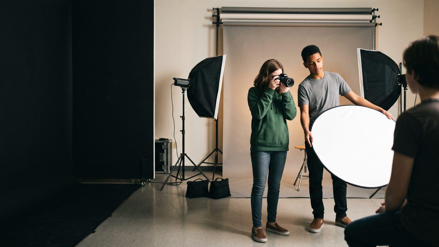 A student photographing a classmate with a DSLR while another adjusts a reflector